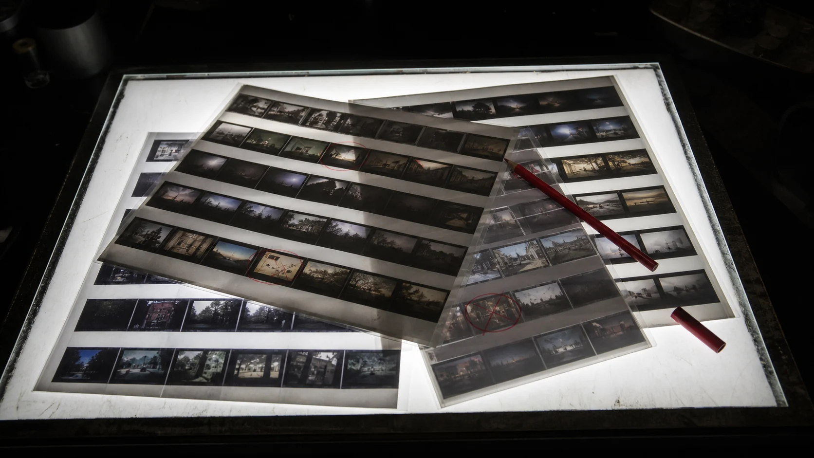 Contact sheets on a lightbox with a red pencil and rejected frames crossed out