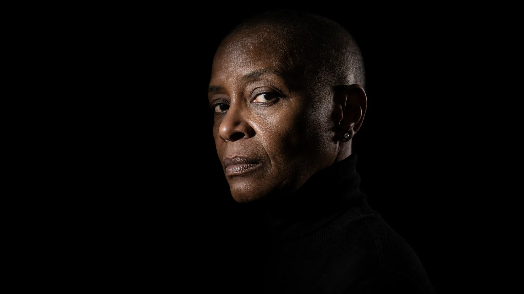 A chiaroscuro portrait of a reviewer looking back over their shoulder against a black background